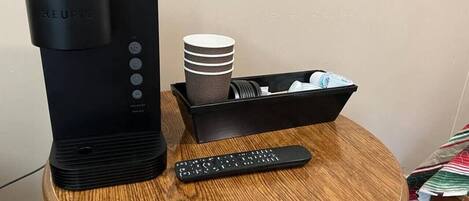 Una cafetera Keurig sobre una mesa de madera, con un control remoto y una pila de tazas blancas.