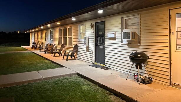 A motel with a covered outdoor seating area, a grill, and a well-lit entrance.