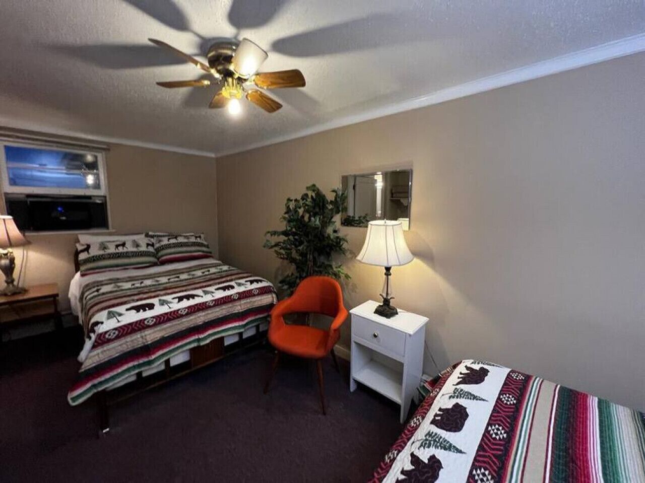A bedroom with two beds, a ceiling fan, a nightstand with a lamp, and a chair.