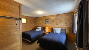 A room with two beds, wooden walls, a small table with a lamp, and a framed picture on the wall. - Lyons in Onaway - 2 Full Beds - Room 2 - Sleeps 4 (Onaway)