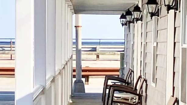 A covered outdoor seating area with wooden chairs and tables, overlooking a beach. - Hampton Beach Getaway | Mins to Portsmouth+ Maine (Hampton)