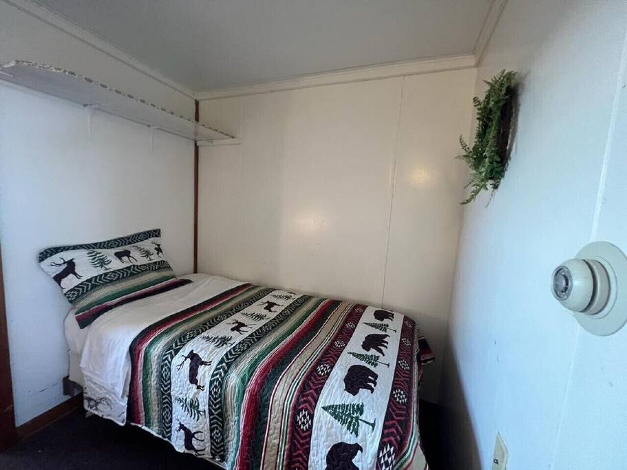 Habitación pequeña con cama individual, pared blanca sencilla y puerta con pomo redondeado.