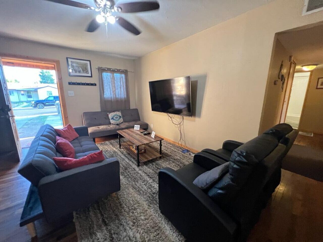 Un salon comprenant un canapé, un fauteuil inclinable, une table basse et un téléviseur fixé au mur.