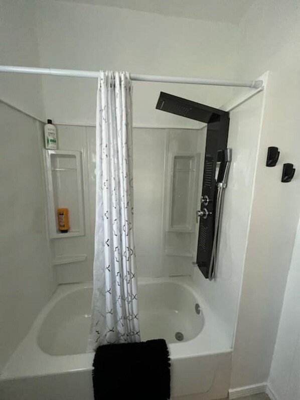 A bathroom with a bathtub, a shower curtain, and a towel rack. - The Western Roost | A Vensérra Retreat Near Hot Springs State Park (Thermopolis)