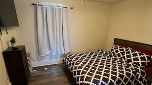 A bedroom with a bed, a ceiling fan, a TV, and a window with curtains. - The Western Roost | A Vensérra Retreat Near Hot Springs State Park (Thermopolis)