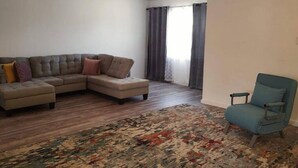 Un salon avec un canapé d’angle, un tapis à motifs et un fauteuil turquoise.