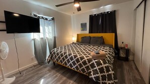 Une chambre à coucher avec un lit, un ventilateur de plafond, une télévision et une fenêtre avec des rideaux.