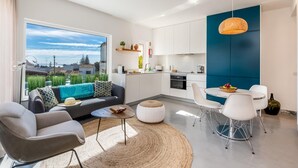 A modern apartment with a living area, kitchen, and dining space. It features a large window with a view of greenery and buildings.