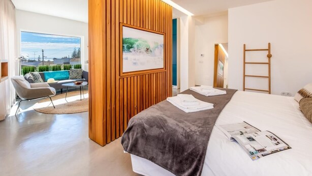 A modern hotel room with a bed, a wooden accent wall, a view of greenery, and a balcony.