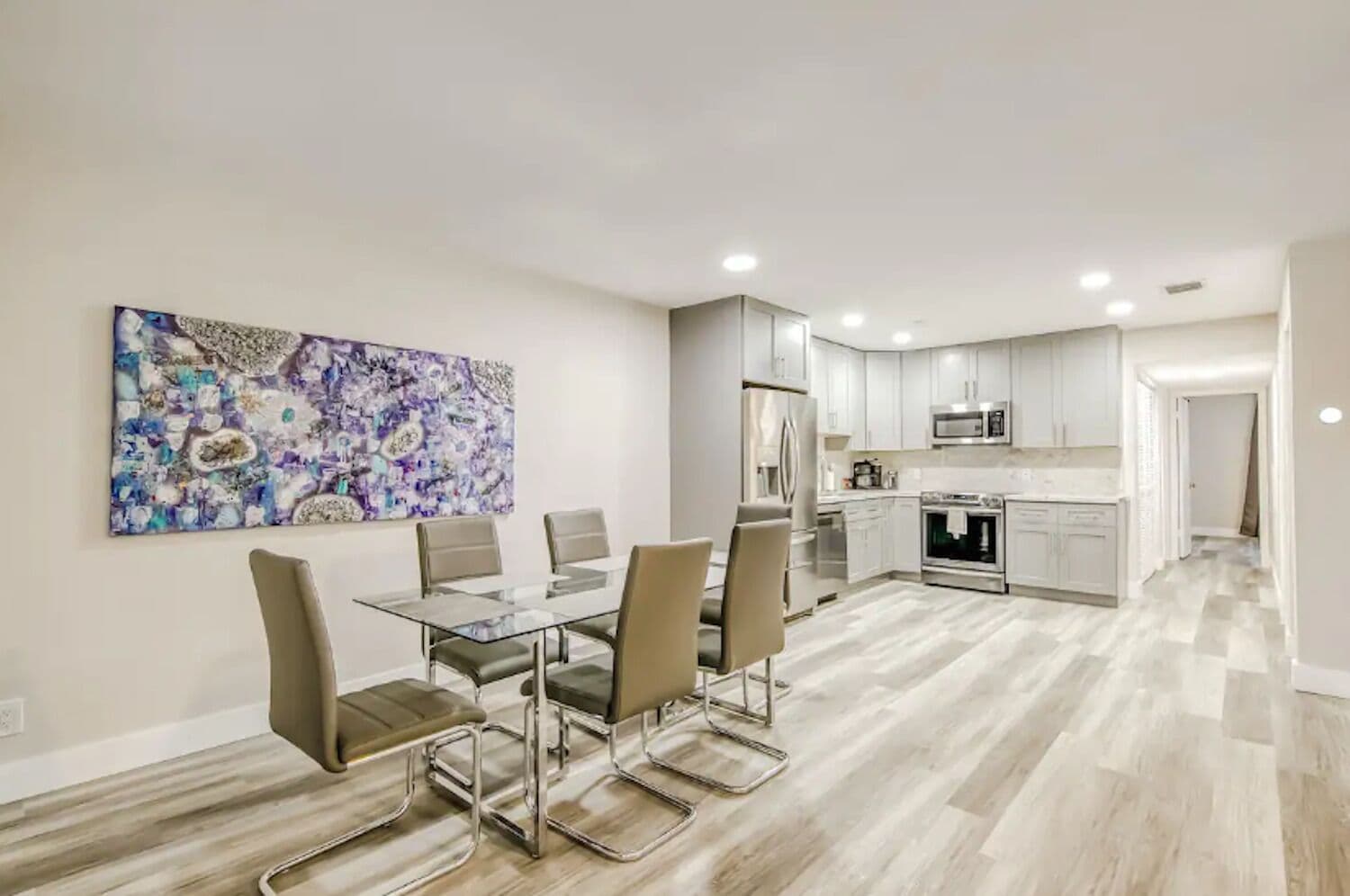 A modern kitchen with white cabinets, stainless steel appliances, and a dining area with a glass table and four chairs.