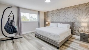 Ein Schlafzimmer mit einem Bett, einem Hängesessel, einem Nachttisch und einem Fenster mit Vorhängen.