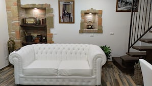 A white tufted sofa in a room with a brick wall, a wooden staircase, and a framed picture on the wall. - Dimora Forgione B&B (Pietrelcina)