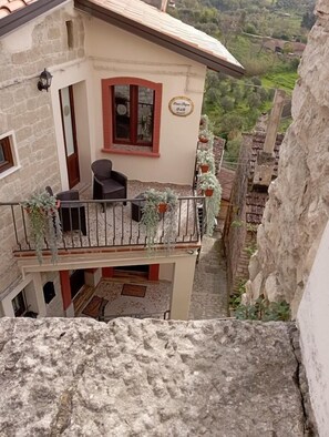 Un edificio de dos pisos con balcón, paredes de piedra y vistas al valle.