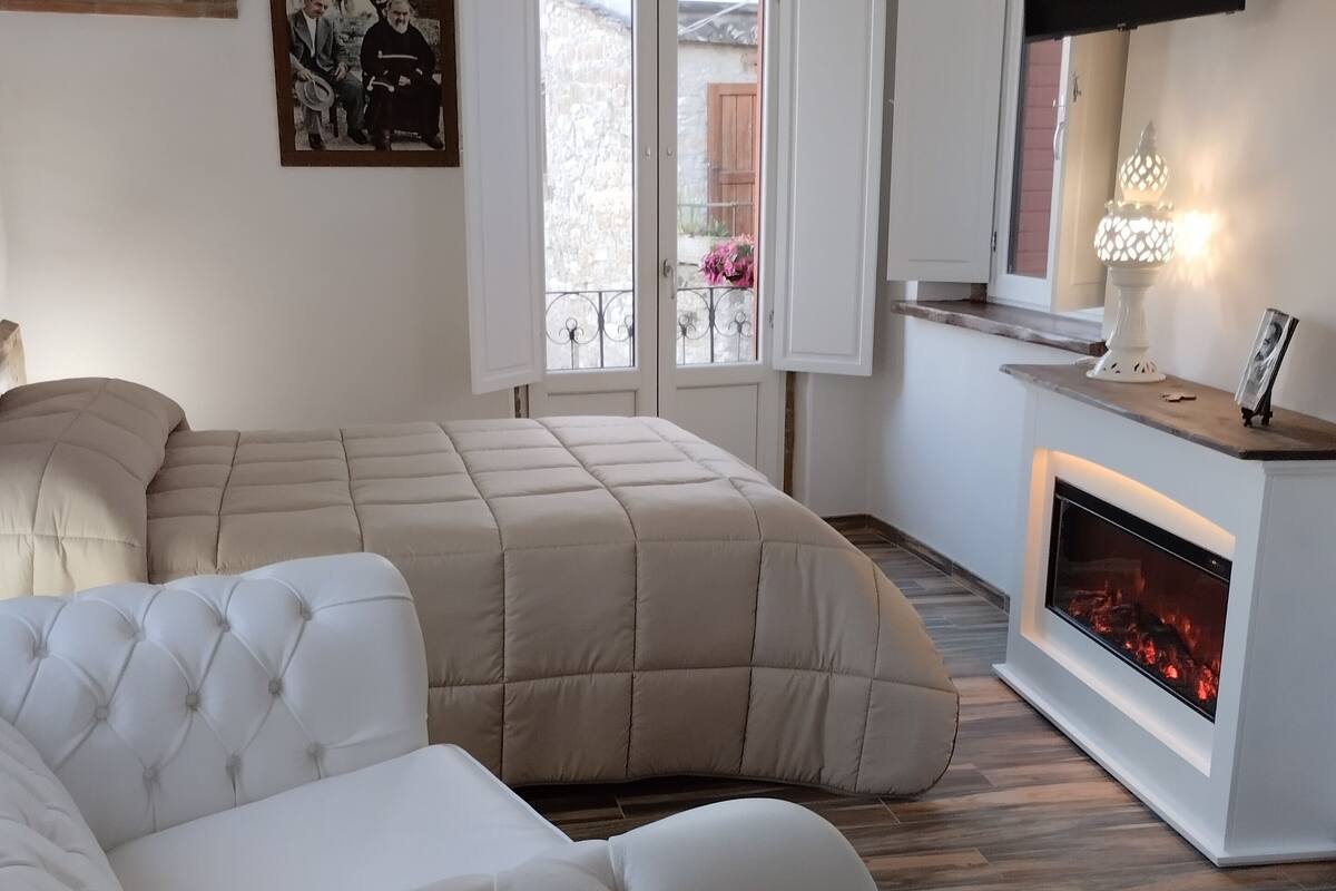 A modern bedroom with a large bed, a sofa, a fireplace, and a TV mounted on the wall.