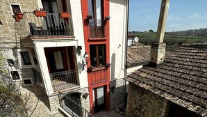 A two-story building with a stone facade, red accents, and a small balcony with a metal railing. - Dimora Forgione B&B (Pietrelcina)