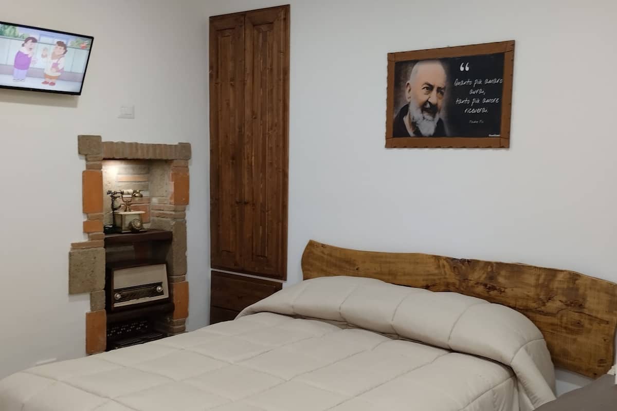 A bedroom with a bed, a wooden headboard, a fireplace, a television, and a poster on the wall.