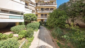 Un sendero estrecho bordeado por follaje y un edificio de varios pisos con balcones.