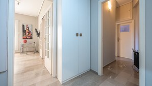 Un pasillo con pared azul claro, una puerta con un pequeño ventanal y una lámpara en la pared.