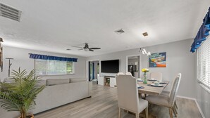 Een moderne woonkamer met een bank, een eettafel en stoelen, een televisie en een plafondventilator.