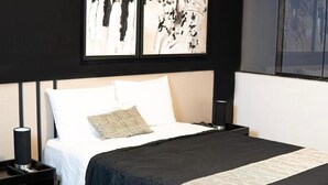 Una cama bien hecha con colcha blanco y negro, una sola almohada y una mesita de noche con una lámpara.