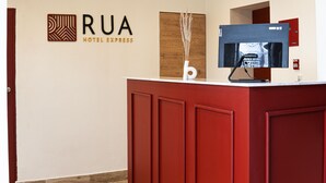 Zona de recepción de un hotel con un mostrador rojo, un monitor y un letrero que dice 'RUA HOTEL EXPRESS'.