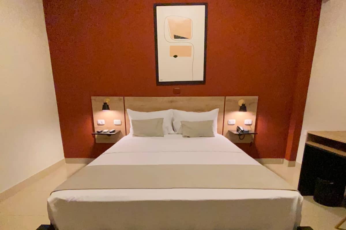 Habitación de hotel con una cama grande, dos mesitas de noche con lámparas, un cuadro enmarcado en la pared y una pared de acento roja.