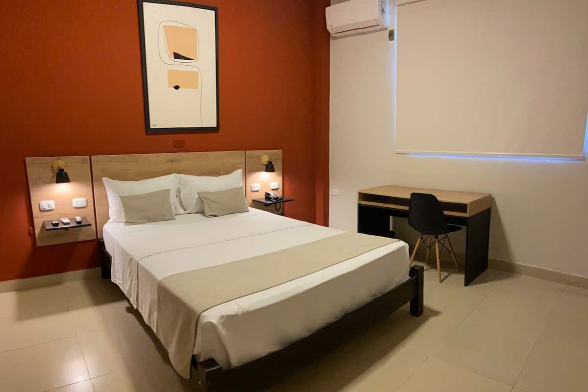 Una habitación de hotel con cama, mesitas de noche, escritorio y una silla.