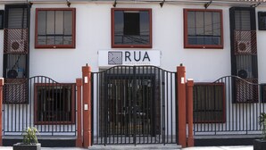 Entrada de hotel con un camino de acceso con puerta de reja, un letrero que dice "RUA HOTEL EXPRESS" y dos macetas a cada lado.