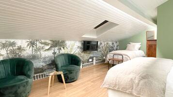 A bedroom with a bed, a chair, a small table, a TV mounted on the wall, and a mural of palm trees.