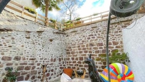 Un espace extérieur entouré de murs en pierre, avec un jacuzzi, un flamant rose gonflable aux couleurs vives et une clôture en bois.