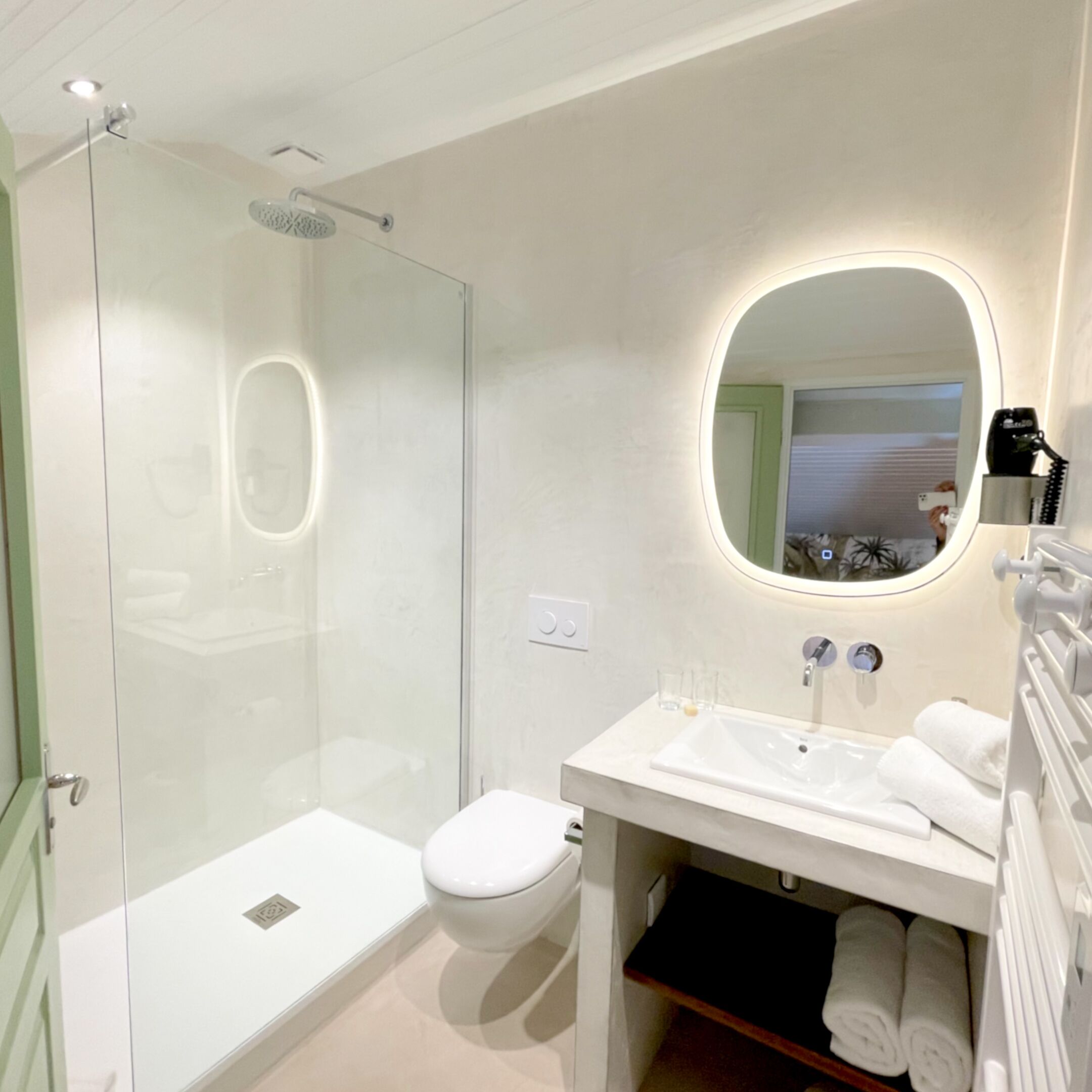 Un baño moderno con ducha envuelta en vidrio, un lavamanos blanco y un espejo de marco redondo.