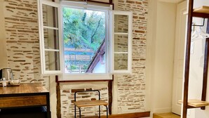 Une pièce avec un mur en pierre, une fenêtre aux volets ouverts, une petite table et une chaise.