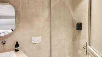 Een badkamer met een douche met glazen wand, een ronde spiegel, een wit wastafelmeubel en een toilet.