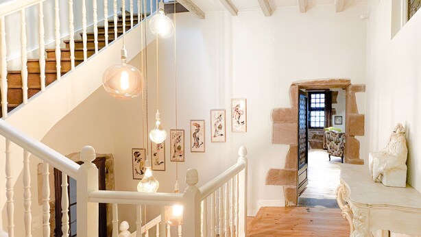 Un escalier avec des balustrades blanches menant à un palier agrémenté de luminaires suspendus et d’œuvres d’art encadrées.