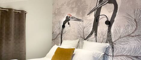 A bedroom with a large bed, white bedding, a brown throw blanket, and a mural of birds on the wall.