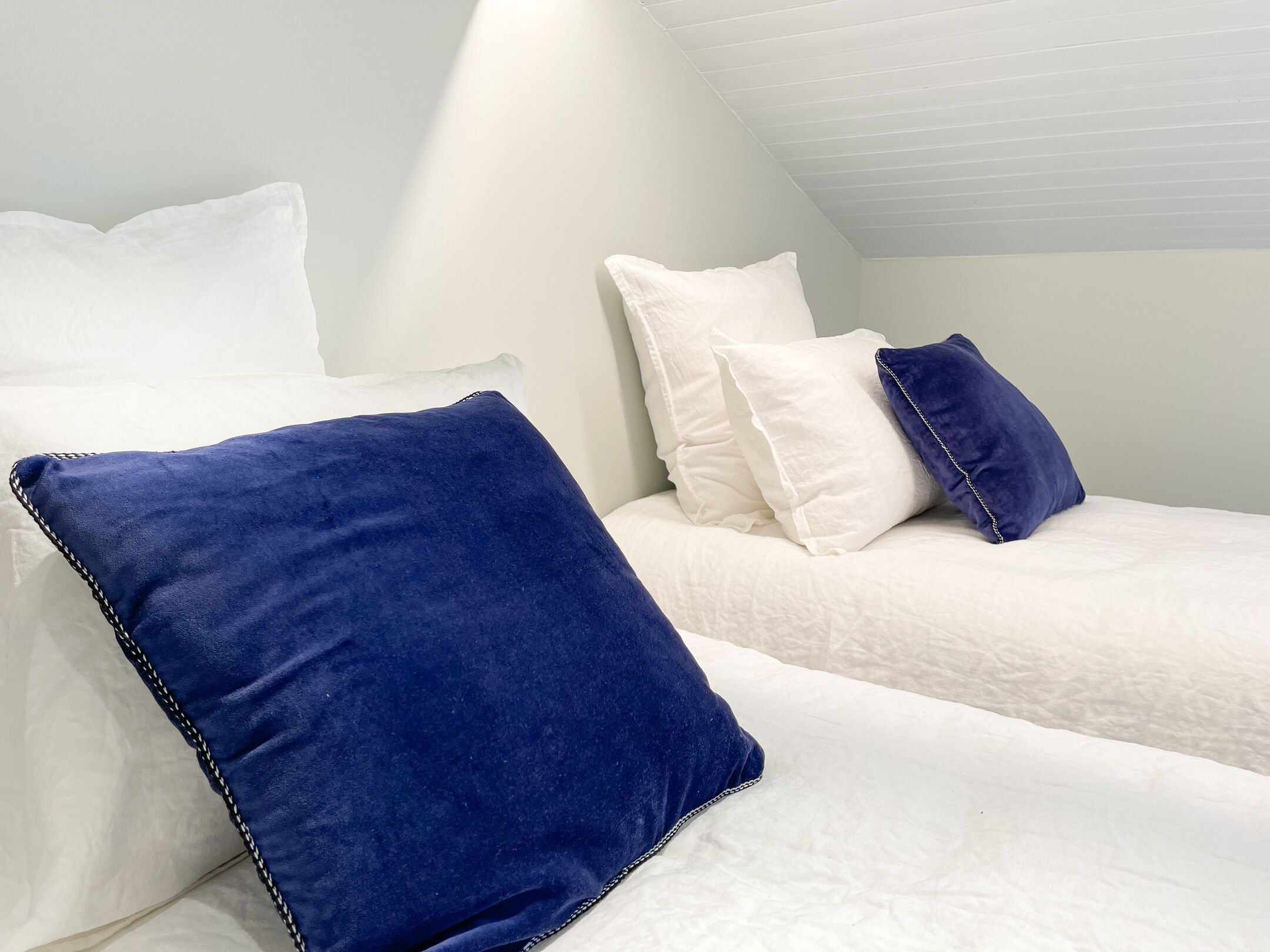 Un dormitorio con dos camas, cada una con ropa de cama blanca y almohadas azules.