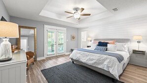Ein Schlafzimmer mit einem Bett, einem Deckenventilator, einem Schminktisch und einem Fenster mit Jalousien.