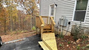 A wooden deck leading to a house with a stone foundation, surrounded by a forested area. - The Bear Den - Jasper Georgia (Jasper)
