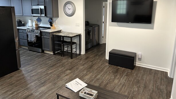 A modern kitchen with grey cabinets, a microwave, and a stove. There is a dining area with a table and chairs, and a TV mounted on the wall. - The Bear Den - Jasper Georgia (Jasper)