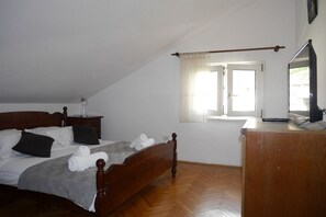Un dormitori amb un llit de fusta, un escriptori amb un ordinador, una finestra amb cortines i un mirall a la paret.