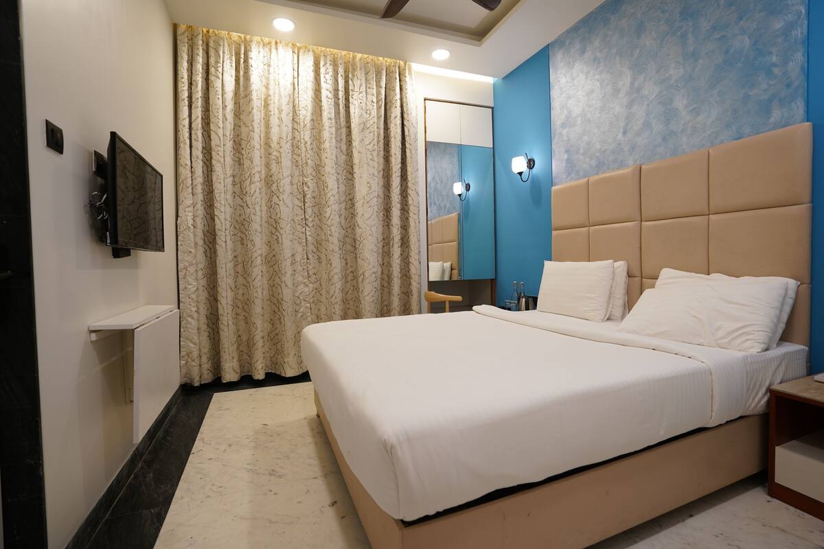 A bedroom with a large bed, a flat-screen TV, a mirror, and a curtain.
