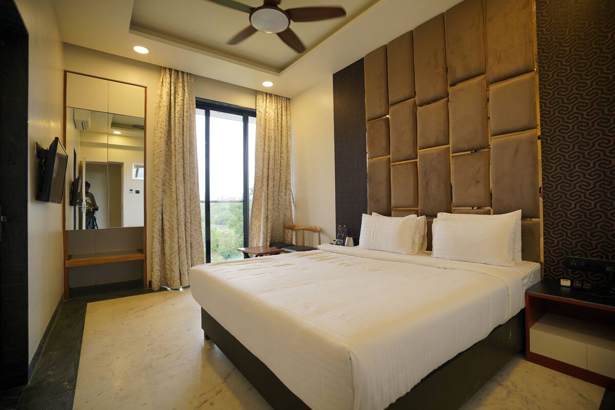 A hotel room with a large bed, a ceiling fan, a nightstand, a mirror, and a view of the outdoors.