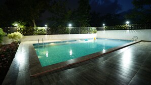 A rectangular swimming pool with a wooden deck surrounding it, enclosed by a fence with lights. - CIESTA TREEO (Mawal)