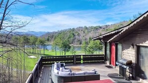A deck with outdoor furniture, a grill, and a view of a lake and forest.