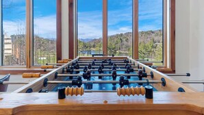 A foosball table in a room with large windows offering a view of a forested landscape.