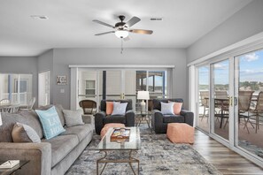 Un salon spacieux doté d’un ventilateur de plafond, de deux canapés, d’une table basse et offrant une vue sur un lac grâce à de grandes portes-fenêtres coulissantes.