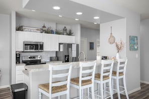A modern kitchen with white cabinetry, a central island with bar stools, stainless steel appliances, and decorative items.