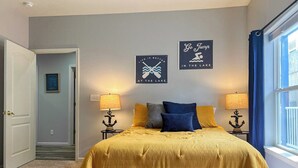 Une chambre à coucher comprenant un lit, deux tables de chevet avec des lampes, une porte, un couloir et deux éléments de décoration murale.