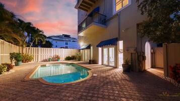 A pool area with a hexagonal tiled floor, a small pool, and a white fence.