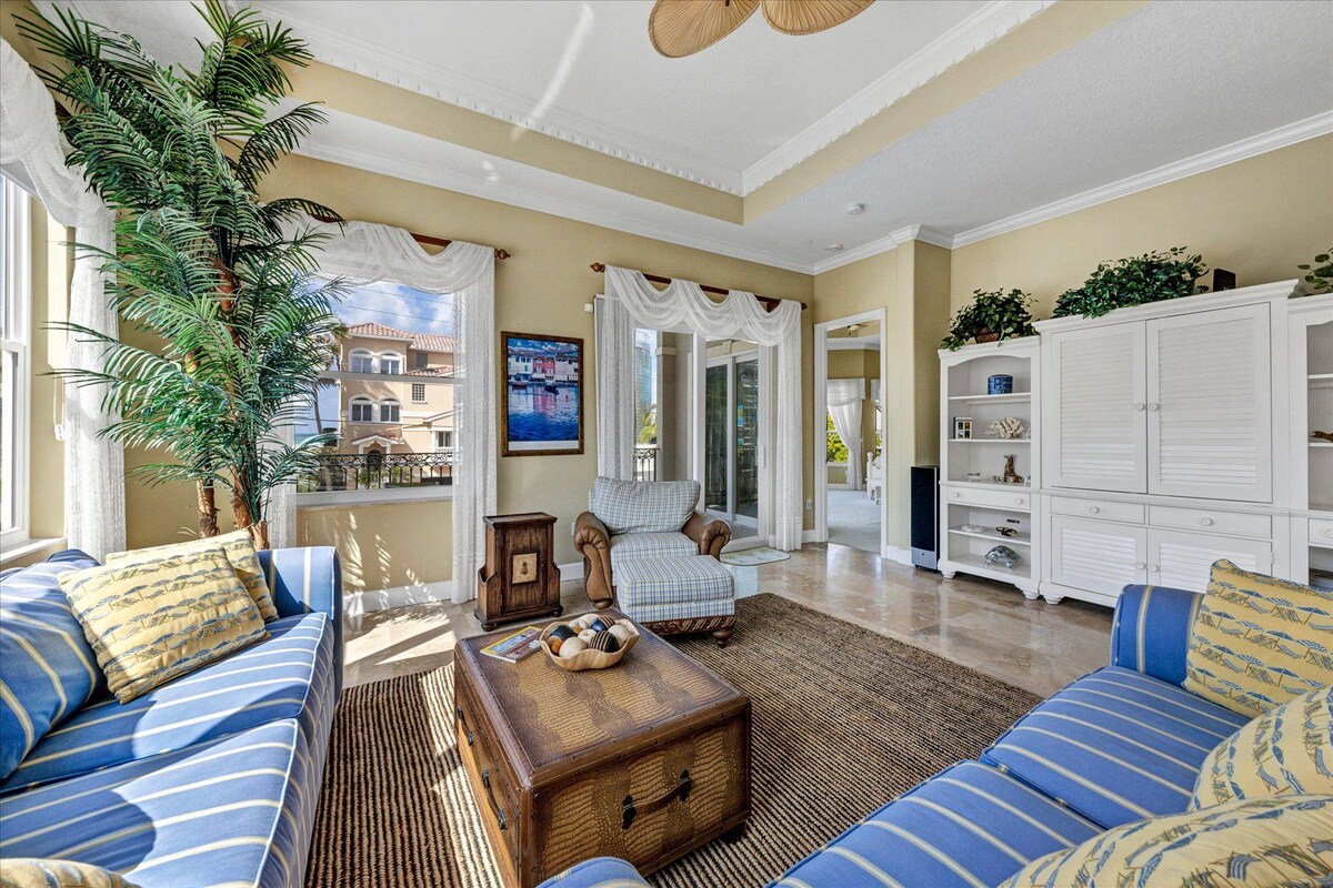 A spacious living room with a large window, a sofa set, a coffee table, and a white cabinet.